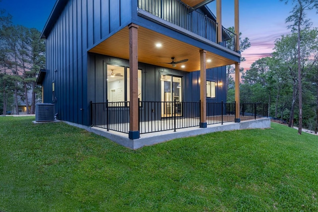 back of house at dusk with a lawn, a balcony, a patio area, and board and batten siding