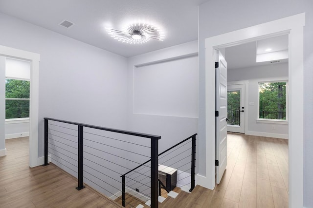 hall with wood finished floors, an upstairs landing, visible vents, and plenty of natural light
