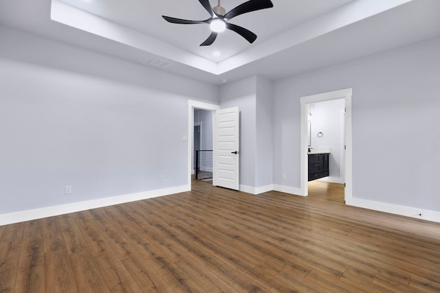 unfurnished bedroom with connected bathroom, a tray ceiling, baseboards, dark wood-type flooring, and recessed lighting