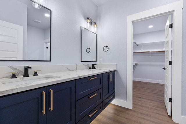 full bath featuring double vanity, wood finished floors, baseboards, and a sink