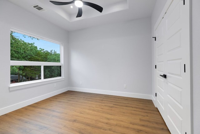 empty room featuring a tray ceiling, wood finished floors, visible vents, baseboards, and ceiling fan