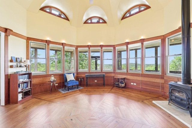 sunroom / solarium with a wooden deck, plenty of natural light, a wood stove, and a towering ceiling