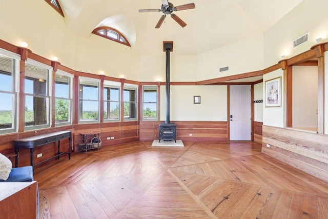 unfurnished living room featuring high vaulted ceiling, a ceiling fan, plenty of natural light, a wood stove, and visible vents