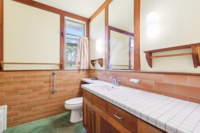 bathroom with tile walls, toilet, vanity, and a wainscoted wall