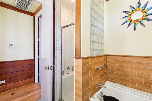 bathroom featuring a wainscoted wall, a bathtub, tile walls, visible vents, and walk in shower
