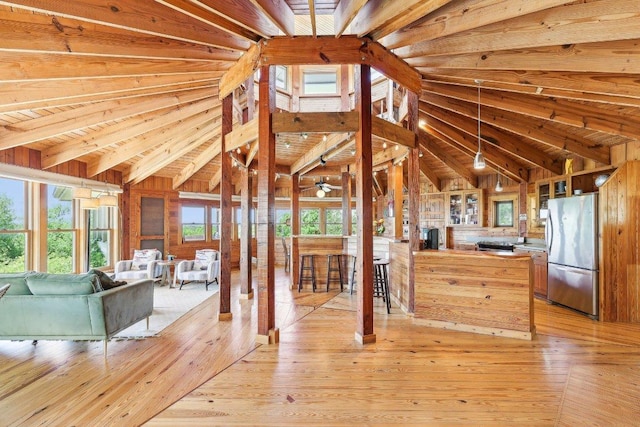 interior space with lofted ceiling with beams, light wood-style flooring, open floor plan, freestanding refrigerator, and wooden walls