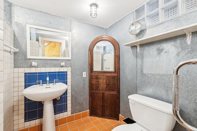 bathroom with a sink, toilet, tile patterned floors, and tile walls