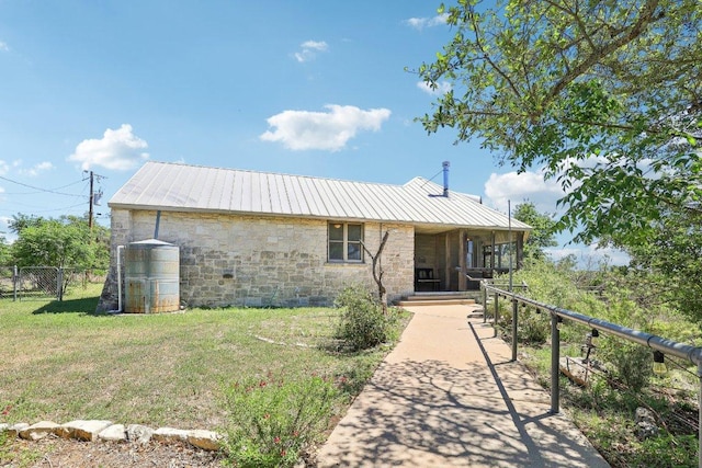 back of house featuring metal roof, a lawn, stone siding, and fence