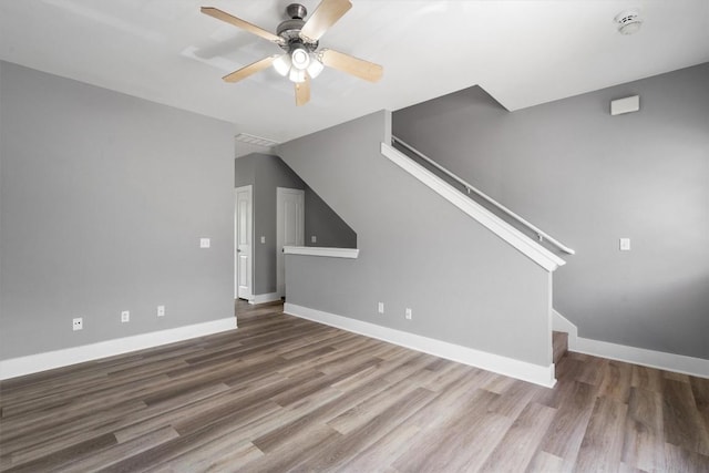 unfurnished living room featuring stairway, baseboards, wood finished floors, and ceiling fan