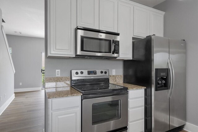 kitchen with light wood-type flooring, appliances with stainless steel finishes, baseboards, and white cabinetry