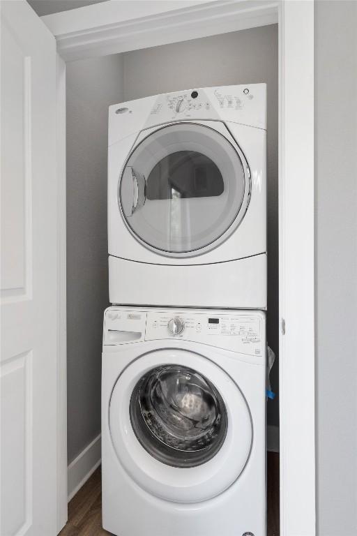 washroom with stacked washer and clothes dryer, wood finished floors, baseboards, and laundry area