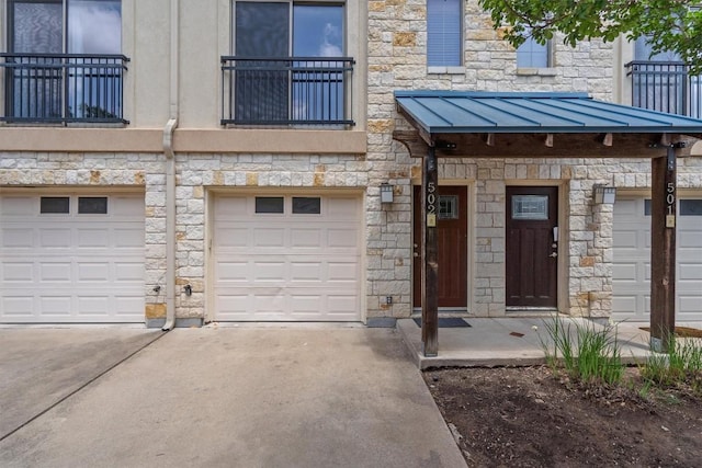 exterior space with driveway, stone siding, a balcony, and a garage