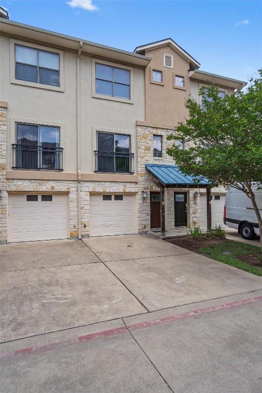 townhome / multi-family property with stone siding, an attached garage, driveway, and stucco siding