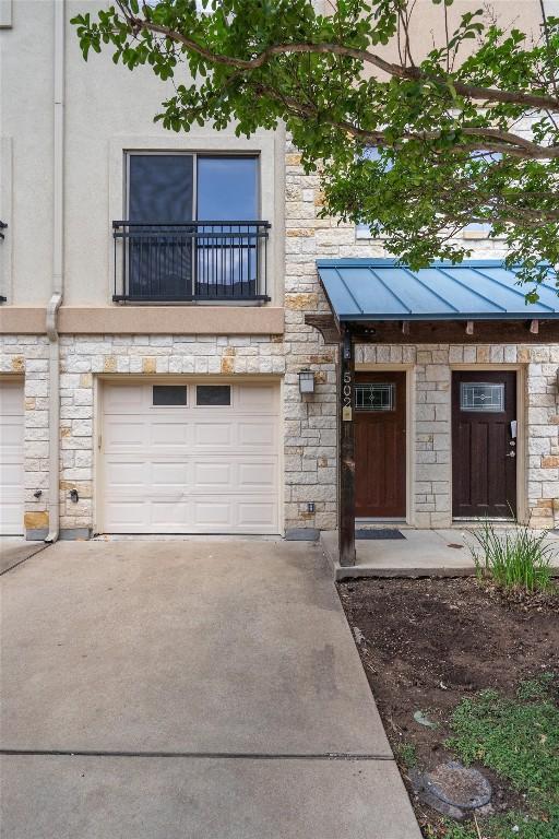 view of front of property featuring stone siding, an attached garage, driveway, and a balcony