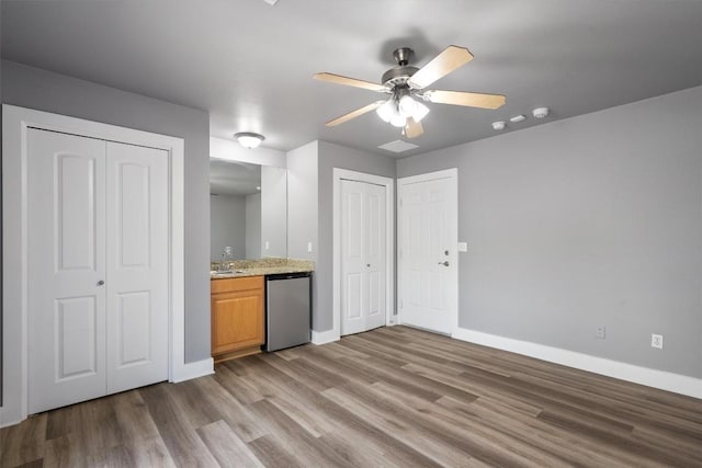unfurnished living room featuring wood finished floors, baseboards, ceiling fan, and a sink