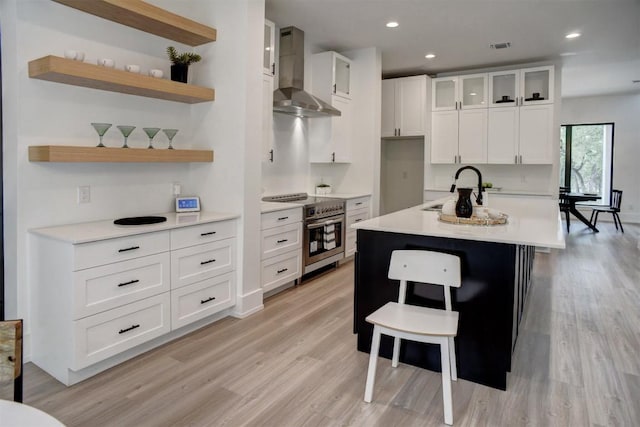 kitchen featuring light wood finished floors, light countertops, a sink, and wall chimney range hood
