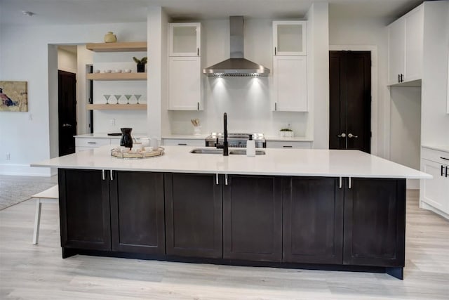 kitchen with wall chimney exhaust hood, a large island with sink, white cabinets, and a sink