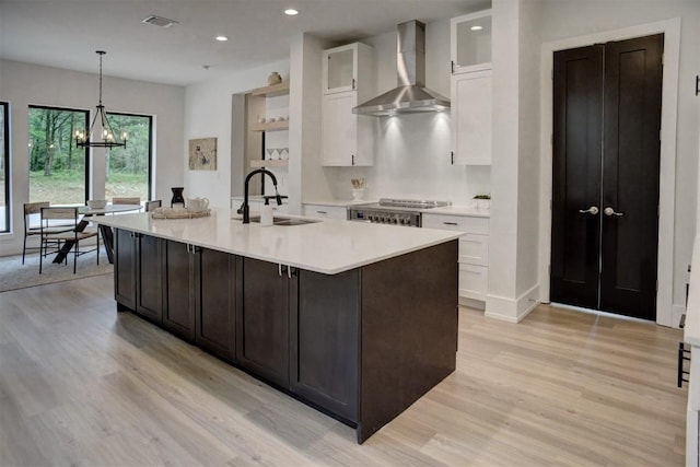 kitchen featuring wall chimney range hood, a sink, light wood finished floors, light countertops, and visible vents