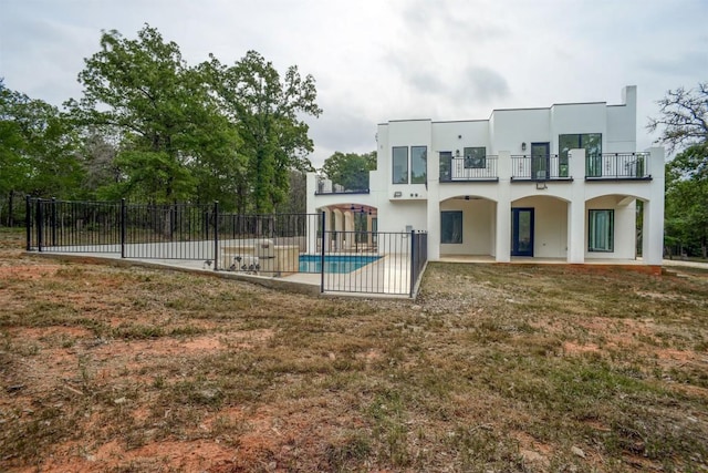 rear view of house with a fenced in pool, fence, a balcony, stucco siding, and a patio area