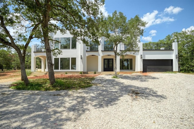 view of front facade featuring a balcony, stucco siding, an attached garage, driveway, and french doors