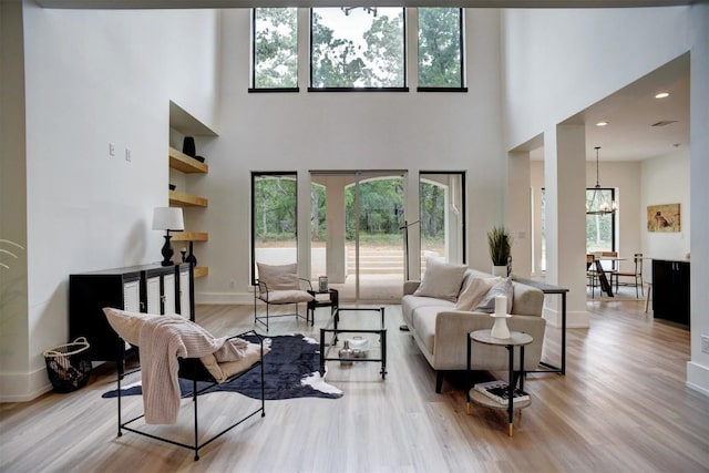 living area with a chandelier, wood finished floors, a towering ceiling, and baseboards
