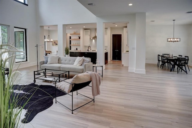 living area featuring baseboards, a notable chandelier, light wood-style floors, and a healthy amount of sunlight