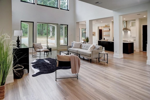living room with light wood-style flooring, visible vents, and a towering ceiling