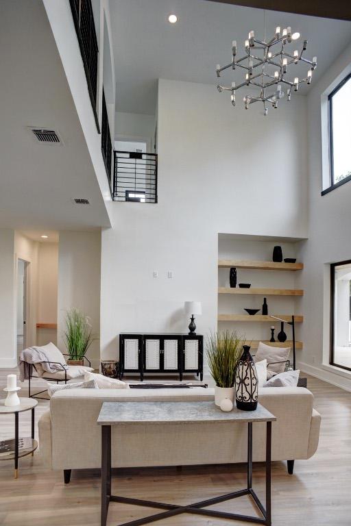 living room with recessed lighting, wood finished floors, visible vents, and a towering ceiling