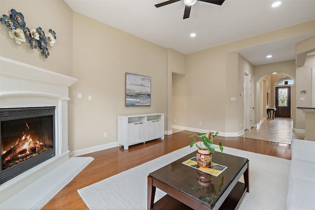 living room with arched walkways, a glass covered fireplace, recessed lighting, a ceiling fan, and wood finished floors