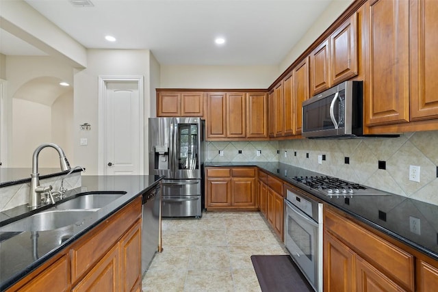 kitchen featuring tasteful backsplash, a sink, brown cabinets, arched walkways, and appliances with stainless steel finishes