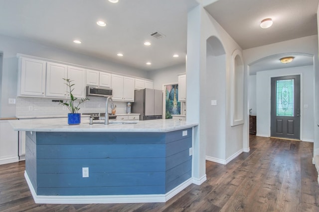 kitchen with tasteful backsplash, arched walkways, stainless steel appliances, white cabinetry, and visible vents