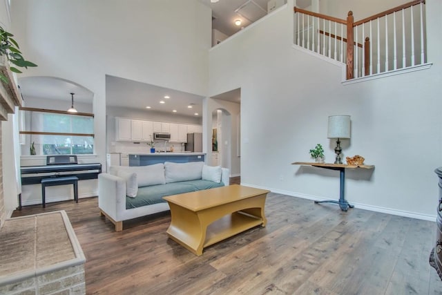 living area featuring arched walkways, a towering ceiling, wood finished floors, and baseboards