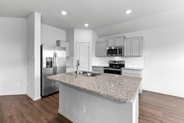 kitchen with a sink, gray cabinets, light stone countertops, an island with sink, and appliances with stainless steel finishes