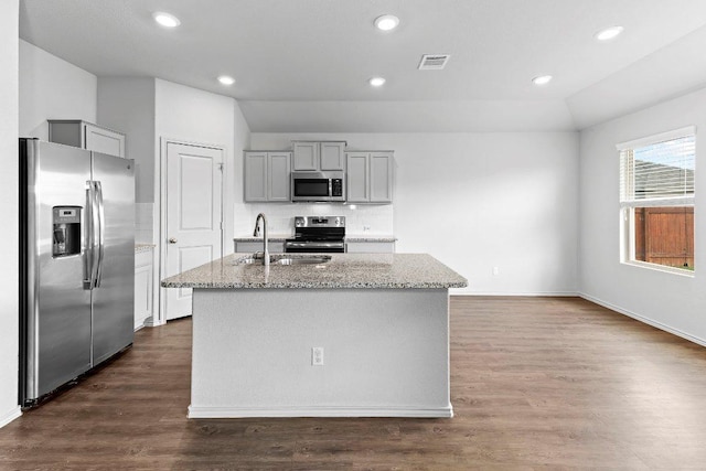 kitchen featuring a sink, gray cabinets, a center island with sink, appliances with stainless steel finishes, and light stone countertops