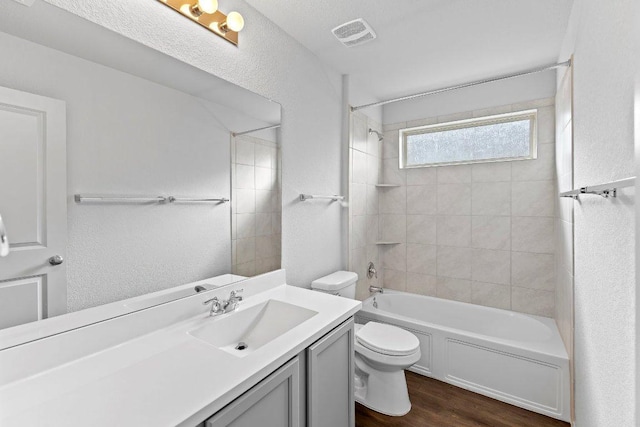 bathroom with wood finished floors, a textured wall, toilet, vanity, and shower / bathtub combination