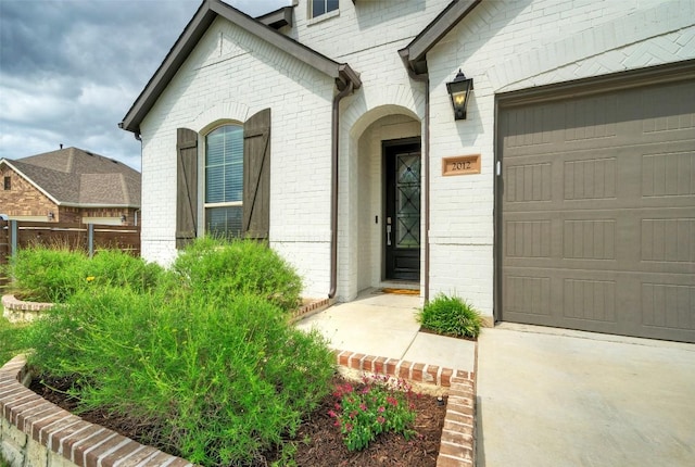 view of exterior entry with an attached garage and brick siding