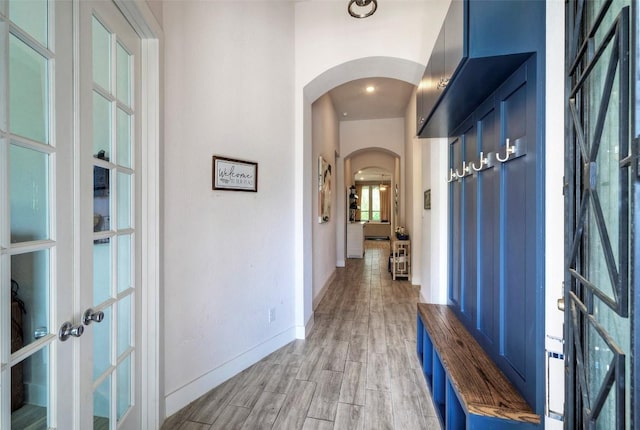 interior space with french doors, light wood-type flooring, baseboards, and arched walkways