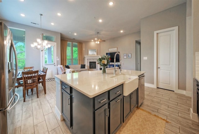 kitchen with a sink, visible vents, stainless steel appliances, a glass covered fireplace, and ceiling fan with notable chandelier