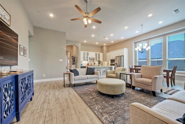 living area with visible vents, light wood-style floors, baseboards, arched walkways, and ceiling fan with notable chandelier