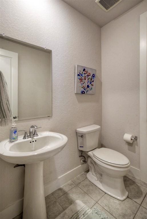 half bathroom featuring a sink, tile patterned floors, toilet, visible vents, and baseboards