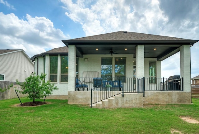 rear view of property with brick siding, fence, roof with shingles, a ceiling fan, and a lawn