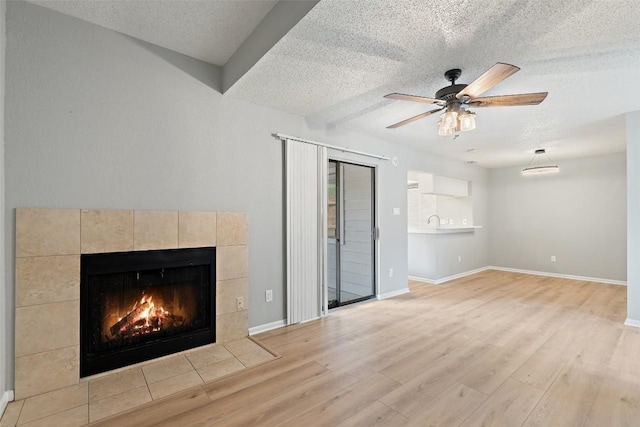 unfurnished living room featuring wood finished floors, ceiling fan, a textured ceiling, and a fireplace