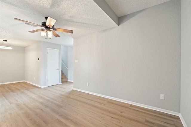 spare room featuring baseboards, stairway, a ceiling fan, and a textured ceiling