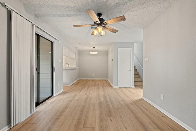 unfurnished living room with stairway, a ceiling fan, light wood-style flooring, and a textured ceiling