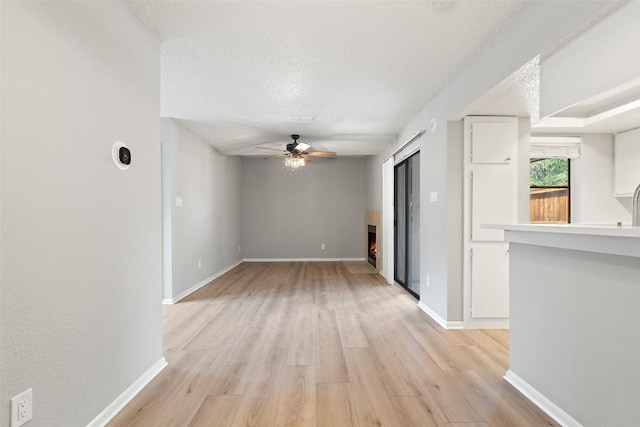 empty room with a lit fireplace, a ceiling fan, a textured ceiling, and light wood-style floors