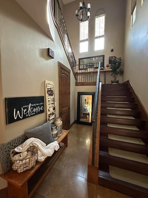 stairway with tile patterned floors, a notable chandelier, and a high ceiling
