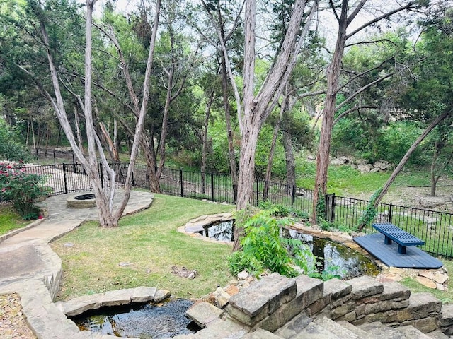 view of yard featuring fence, a deck, an outdoor fire pit, and a small pond
