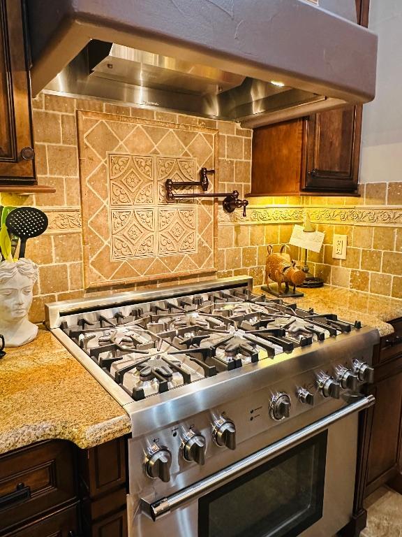 2749 Springwood Ln, Georgetown, TX 78628 - kitchen featuring high end stainless steel range, wall chimney exhaust hood, decorative backsplash, light stone counters, and dark brown cabinets