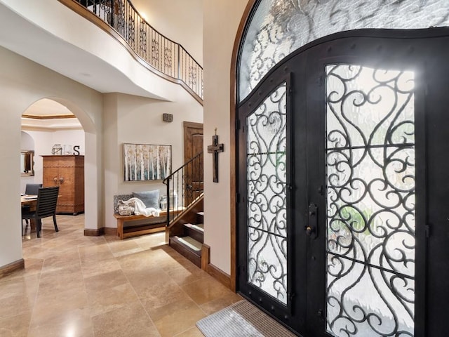 entrance foyer featuring baseboards, arched walkways, stairs, and a towering ceiling