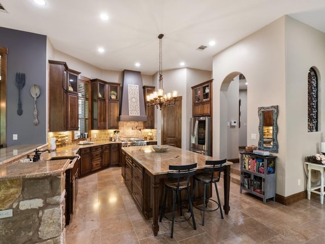 2749 Springwood Ln, Georgetown, TX 78628 - kitchen featuring wall chimney exhaust hood, smart refrigerator, light stone counters, tasteful backsplash, and arched walkways
